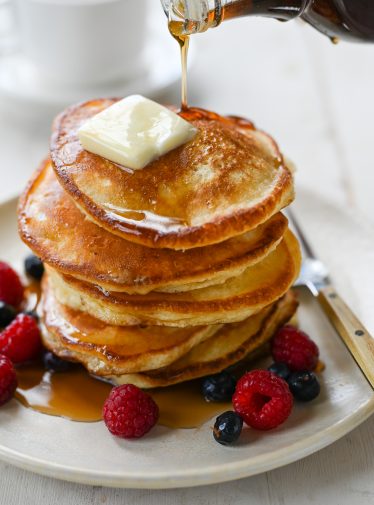 stack of pancakes on plate with berries and maple syrup