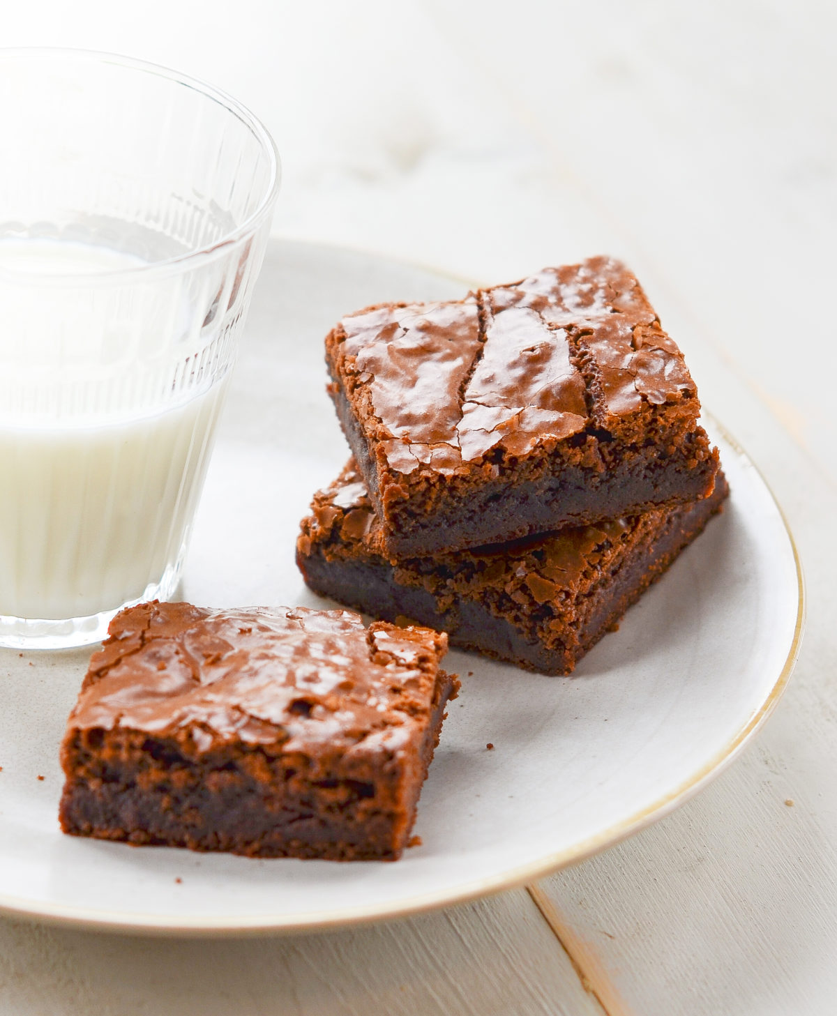 Three brownies on a plate with a glass of milk.