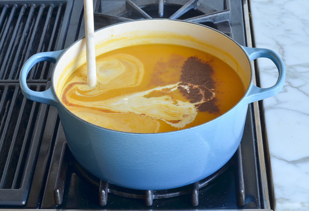 Heavy cream pouring into a Dutch oven of soup.