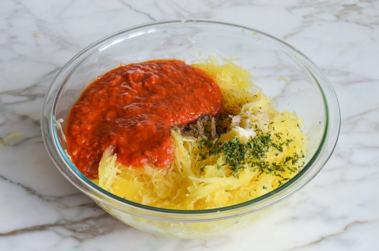 spaghetti squash in bowl with sauce and seasonings