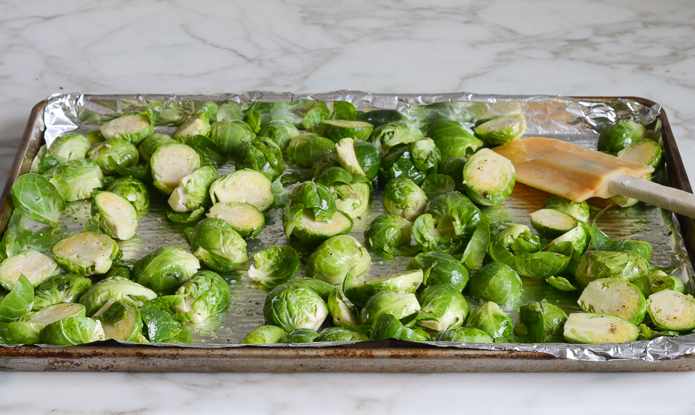 tossing Brussels sprouts with oil, salt, and pepper on lined baking sheet