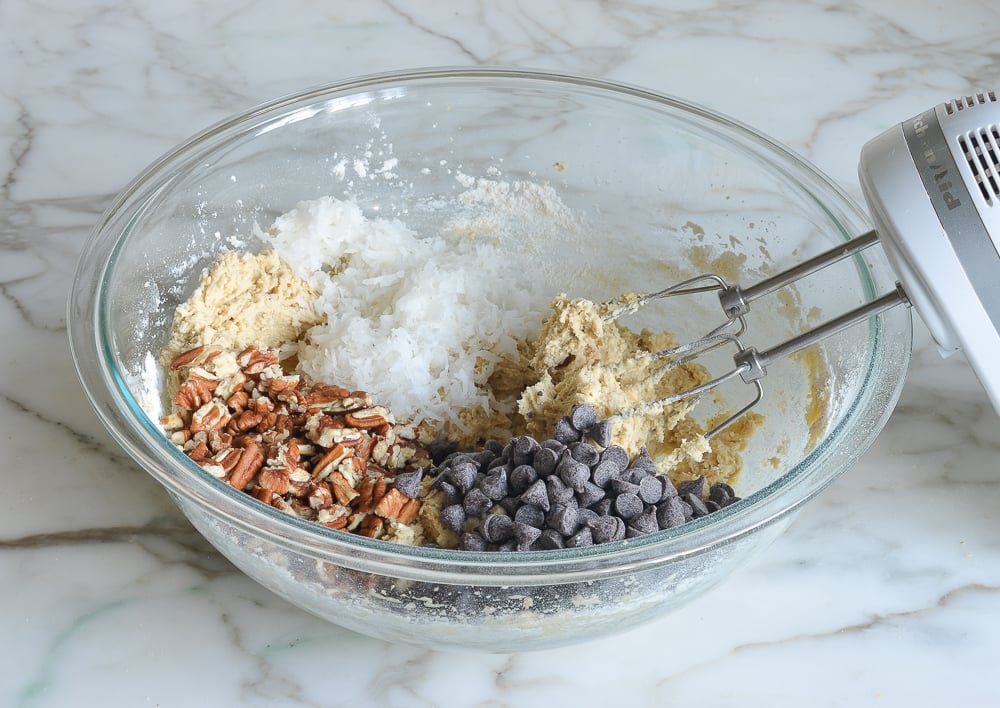 Chocolate chips, coconut, and nuts in a bowl with cookie dough.