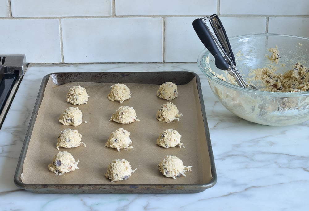 Scoops of chocolate chip cookie dough on a lined baking sheet.