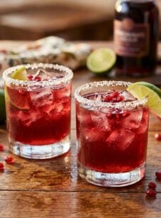 Pomegranate margaritas on wooden table with limes.