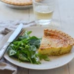 Slice of parmesan and leek quiche on a plate with greens.