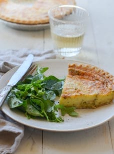 Slice of parmesan and leek quiche on a plate with greens.