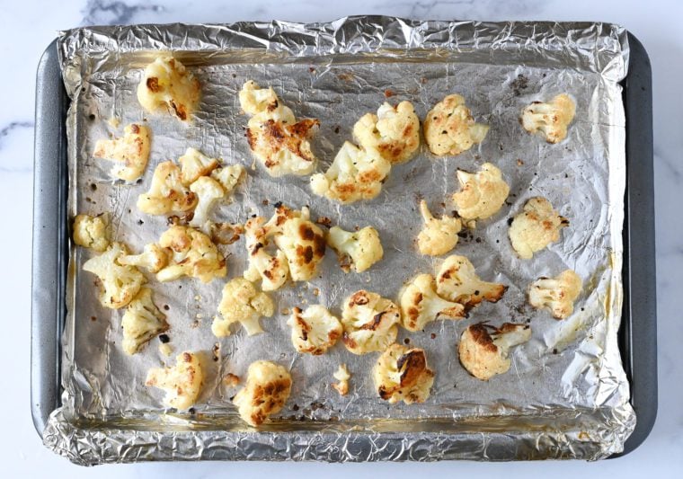 Roasted cauliflower on a lined baking sheet.