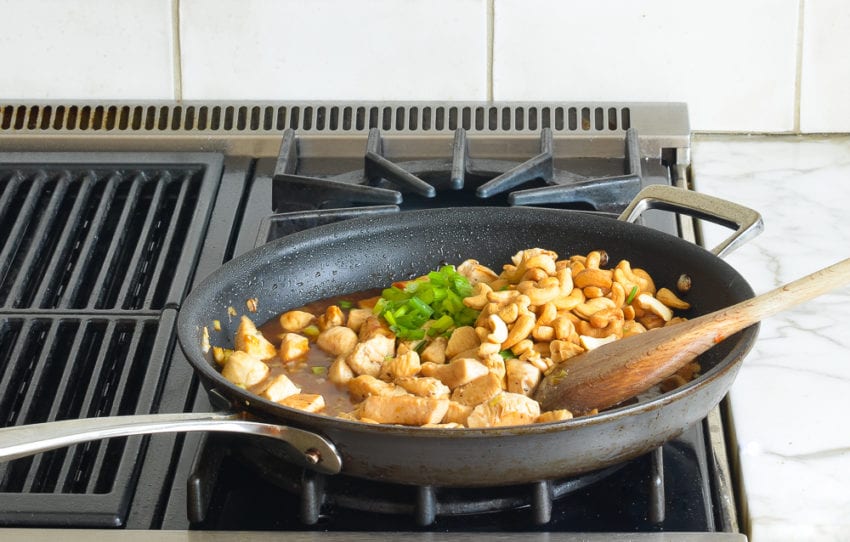 Scallion greens and cashews in a skillet with chicken.
