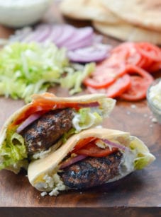 Greek-style lamb burgers on a wooden surface with burger toppings.