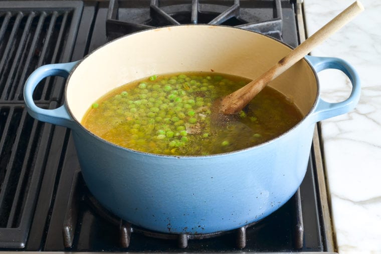 adding broth, peas, and seasoning to pot