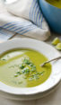 Spoon in a bowl of pea soup with basil.