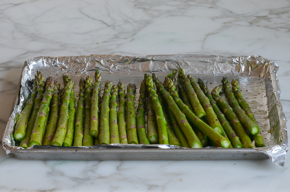 asparagus tossed with oil and seasoning on baking sheet