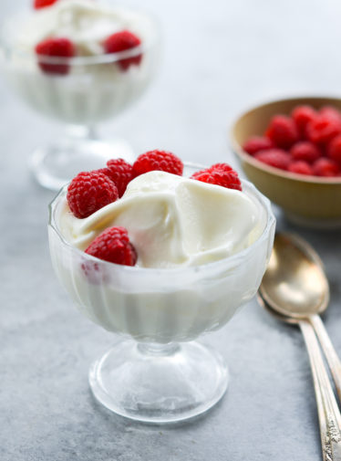 Stemmed glass of frozen yogurt topped with raspberries.
