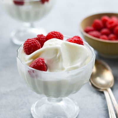 Stemmed glass of frozen yogurt topped with raspberries.