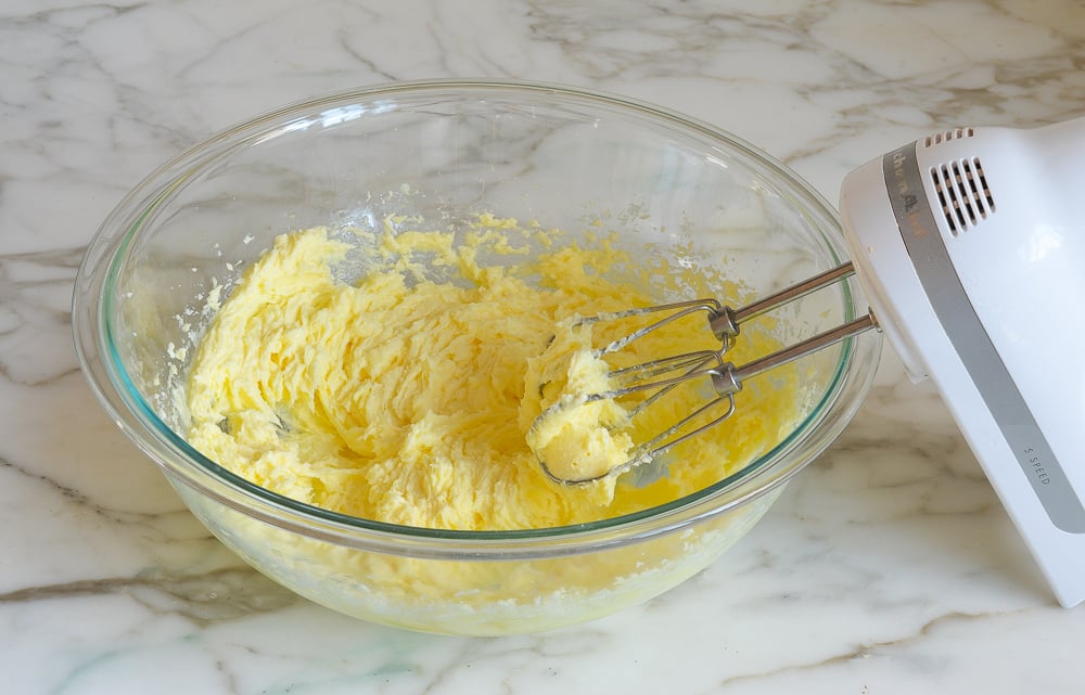Electric mixer in a bowl with a yellow mixture.