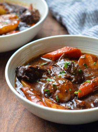 Spoon in a bowl of beef stew with carrots and potatoes.