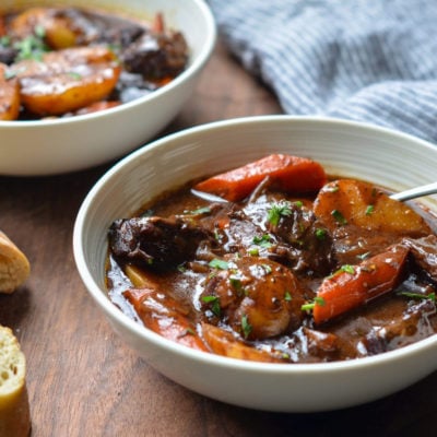 Spoon in a bowl of beef stew with carrots and potatoes.
