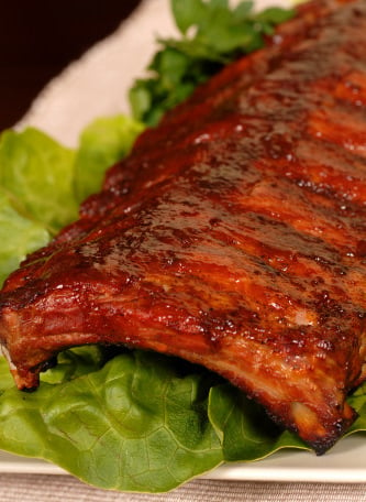 Oven baby back ribs with hoisin barbeque sauce on a plate with greens.