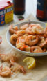 Bowl of peel-and-eat boiled shrimp with cocktail sauce in from of Old Bay Seasoning.