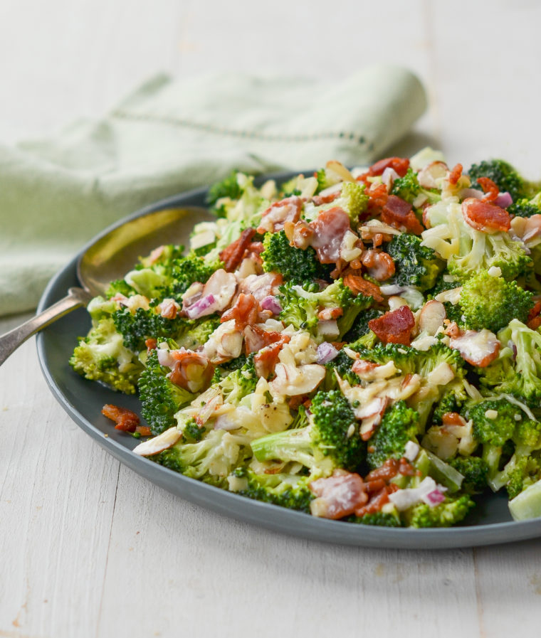 Spoon on a plate of broccoli salad with bacon, cheddar, and almonds.