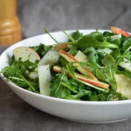 Bowl of arugula salad with apples and manchego in cider vinaigrette.