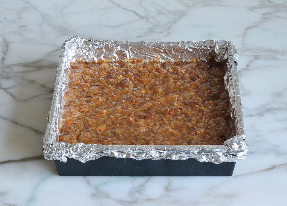 Caramel-colored pecan mixture in a foil-lined baking sheet.