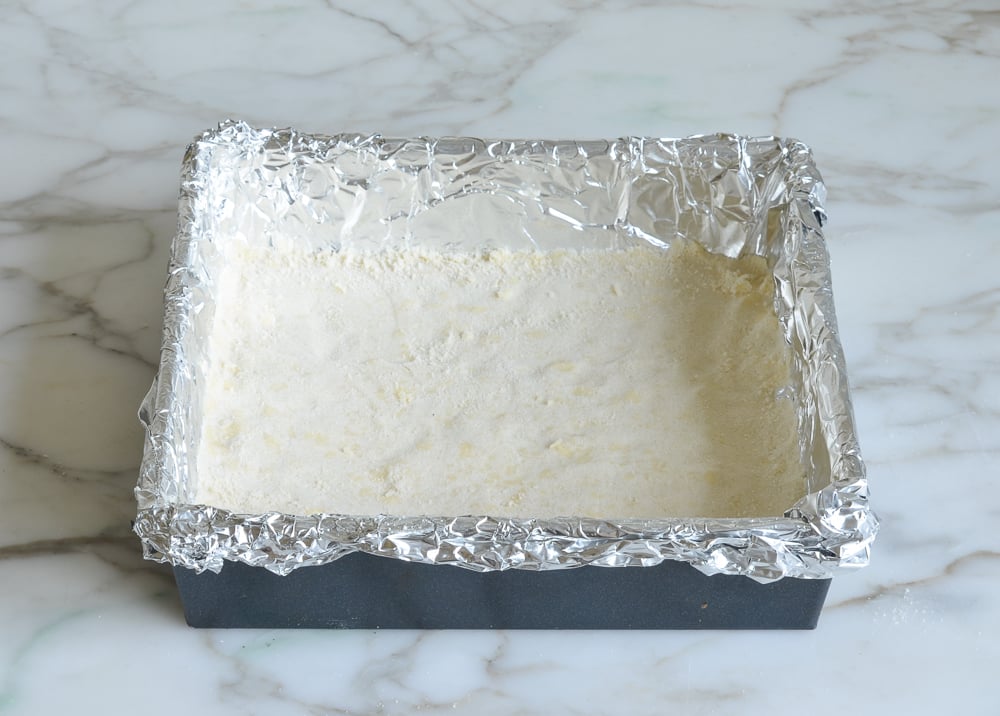 Pressed layer of flour and butter mixture in a foil-lined pan.
