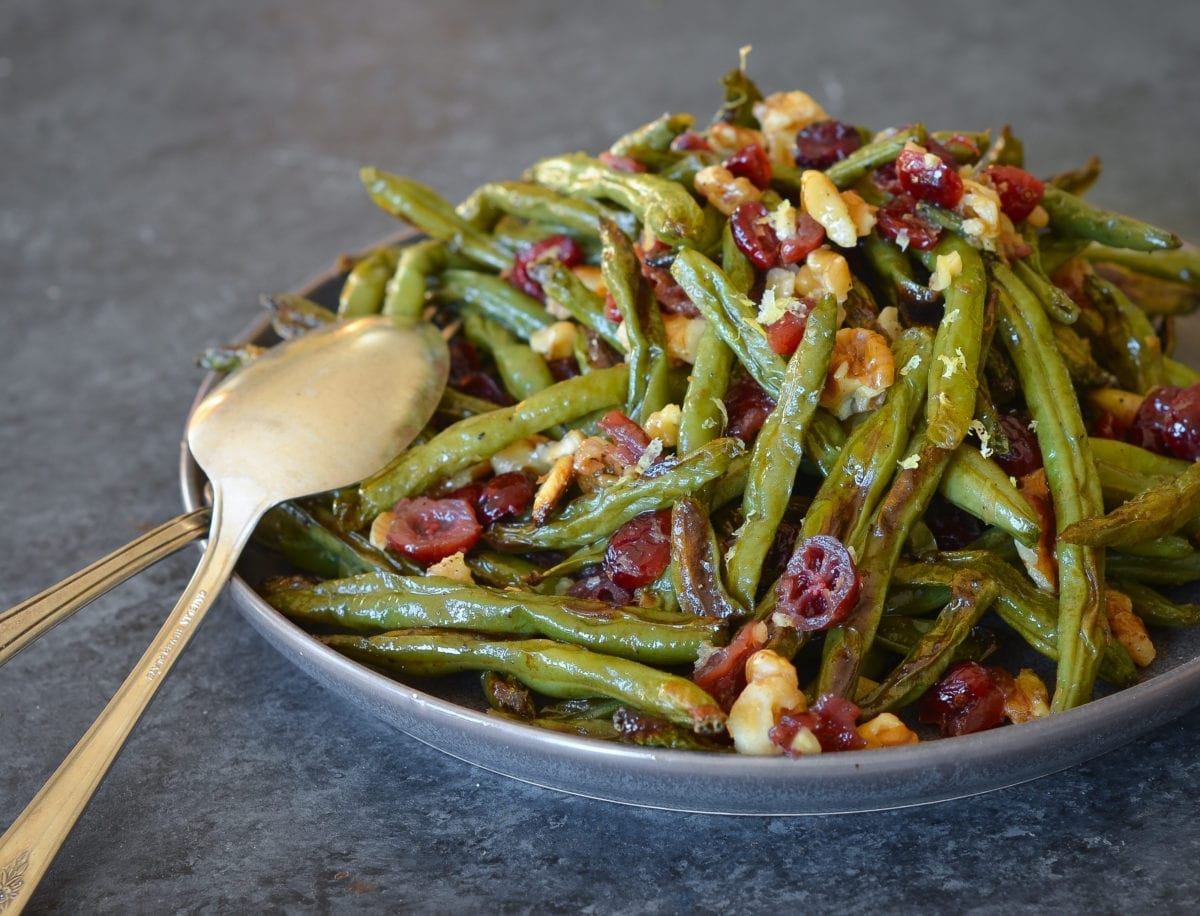 Spoon on a plate with roasted green beans with cranberries and walnuts.