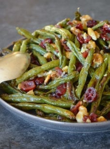 Spoon on a plate with roasted green beans with cranberries and walnuts.