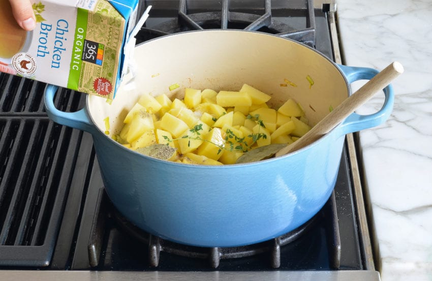 Broth pouring into a Dutch oven with leeks and potatoes.