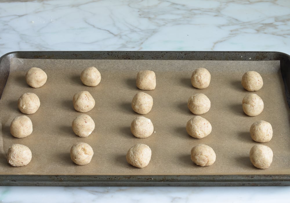 Balls of cookie dough on a lined baking sheet.