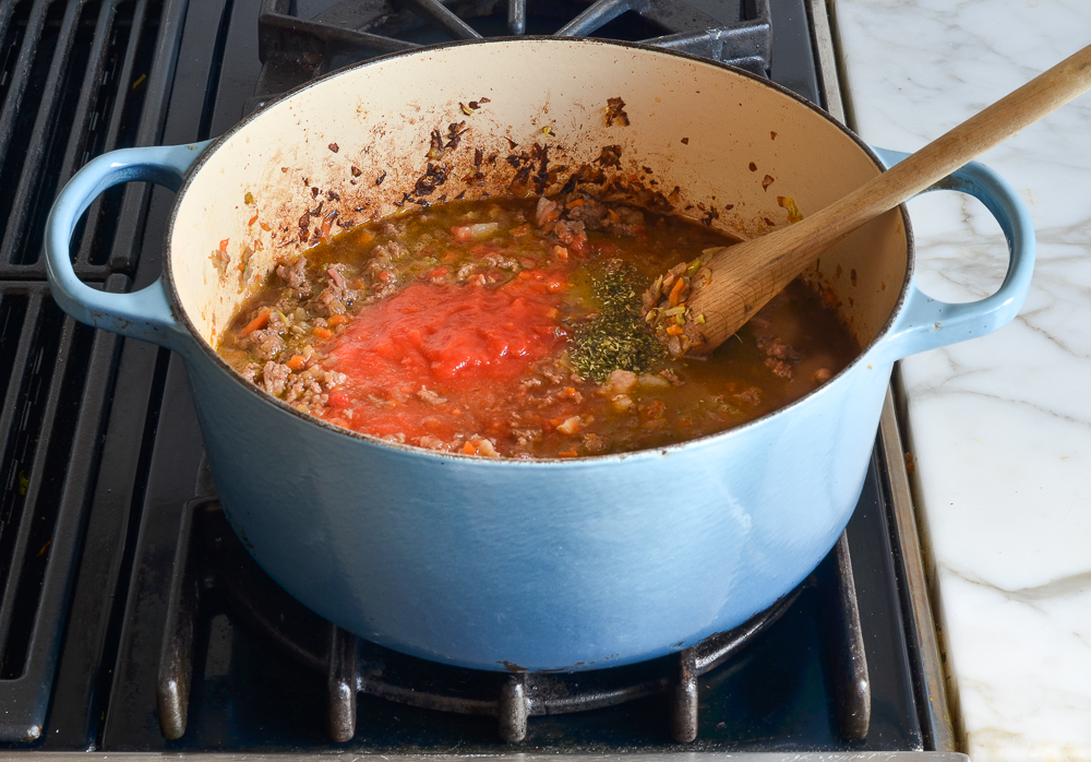 adding broth, tomatoes, and seasoning to the pot