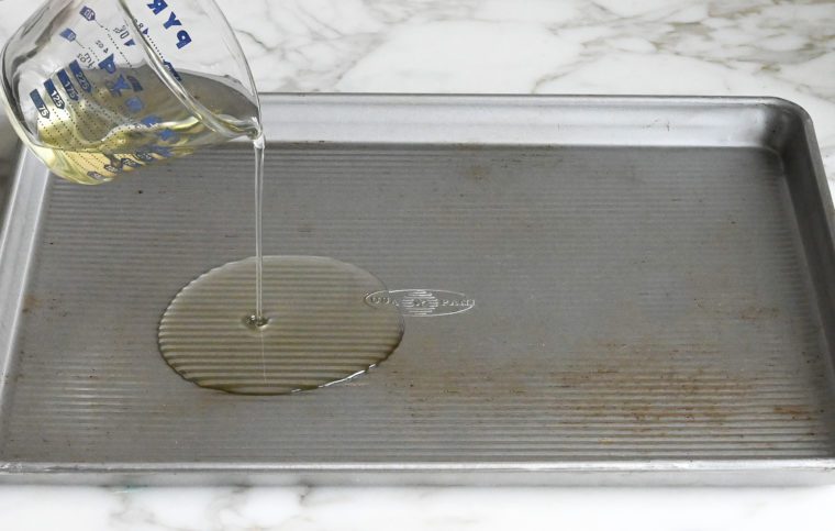 pouring oil in rimmed baking sheet