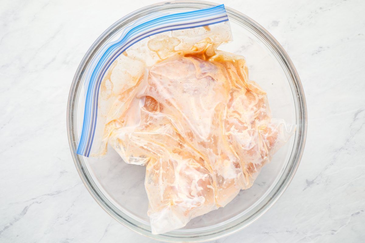 Chicken tenders marinating in seasoned buttermilk, placed in a bag inside a bowl to prevent leakage.