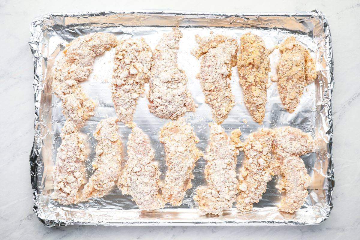Breaded chicken tenders on baking sheet.