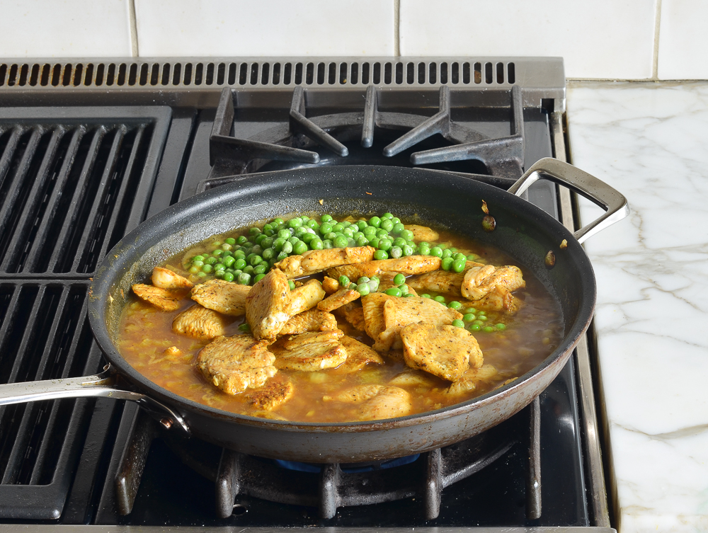 Chicken, peas, chicken stock, and other ingredients in a skillet.
