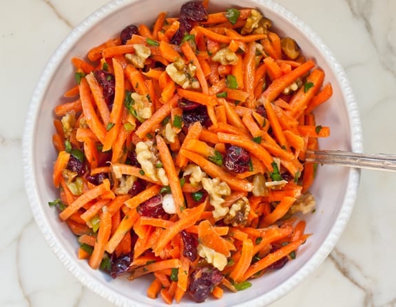 Bowl of carrot slaw with cranberries, toasted walnuts, and citrus vinaigrette.