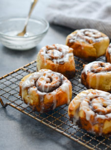 Cinnamon buns with buttermilk glaze on a wired rack.