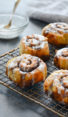 Cinnamon buns with buttermilk glaze on a wired rack.