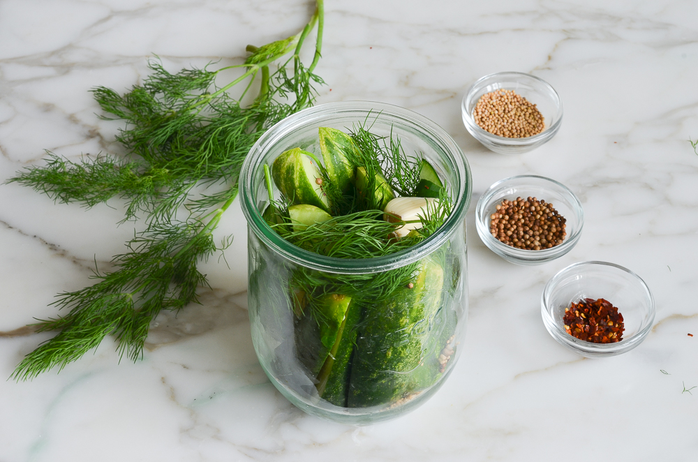 adding cucumbers and spices to jars