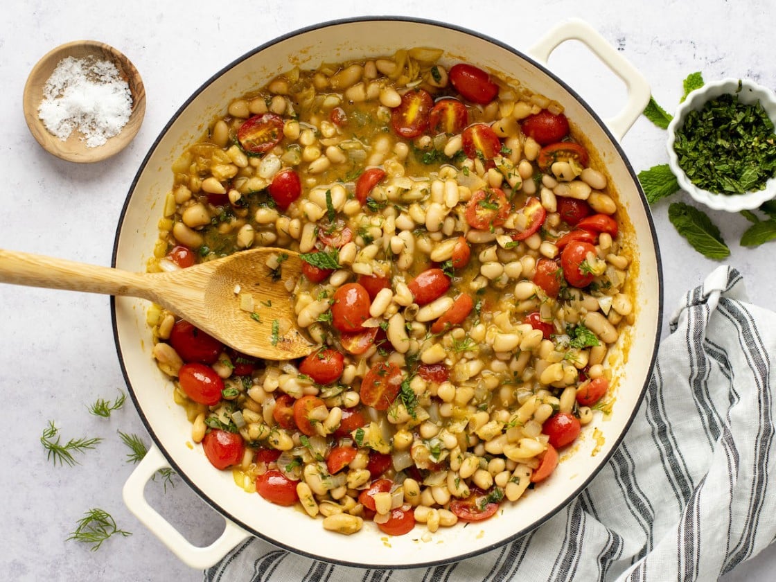 ragout with wood spoon in dutch oven sitting on a striped napkin with small container of salt to the side