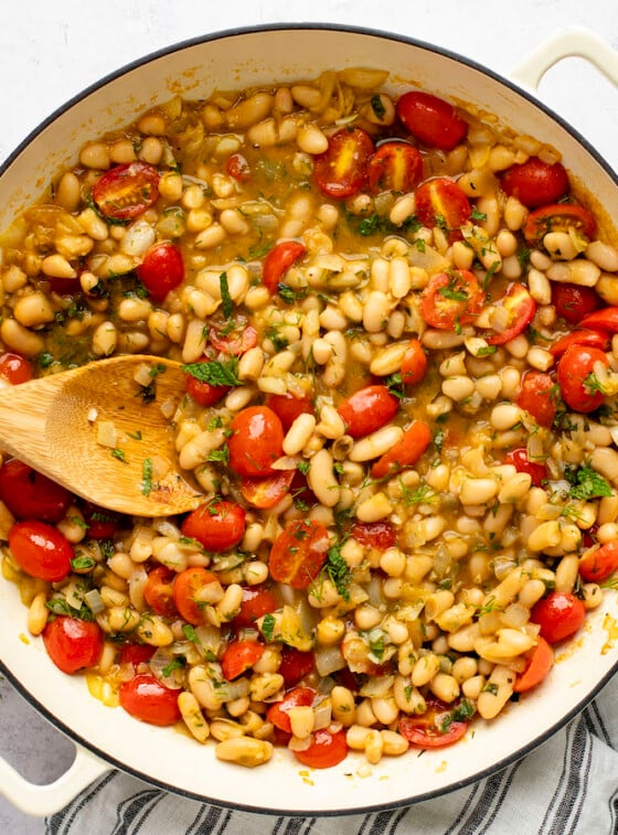 ragout with wood spoon in dutch oven sitting on a striped napkin with small container of salt to the side
