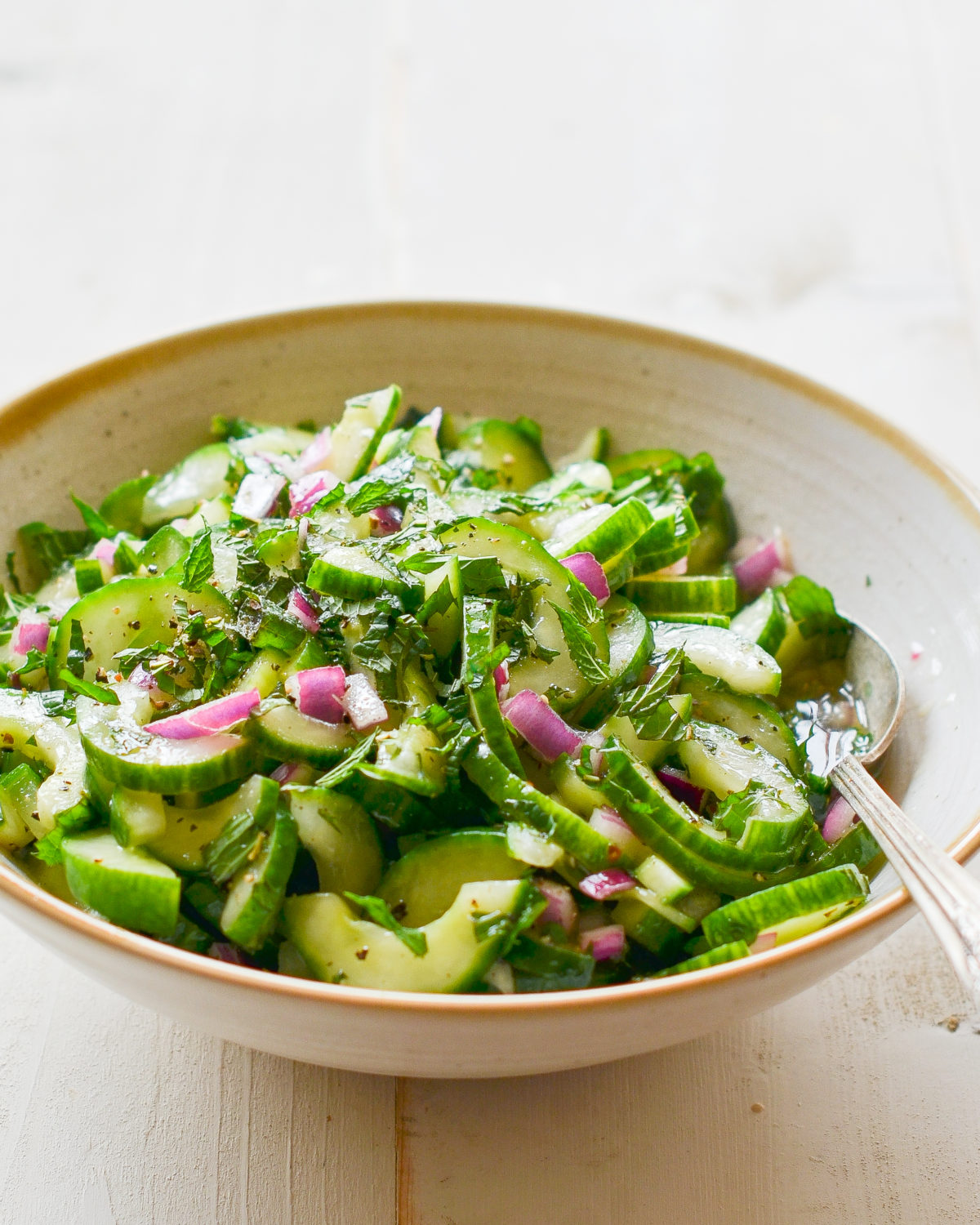 Spoon in a bowl of cucumber salad with mint.