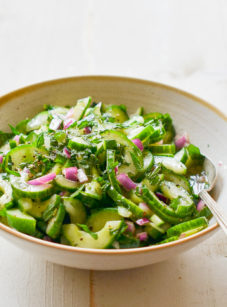 Spoon in a bowl of cucumber salad with mint.