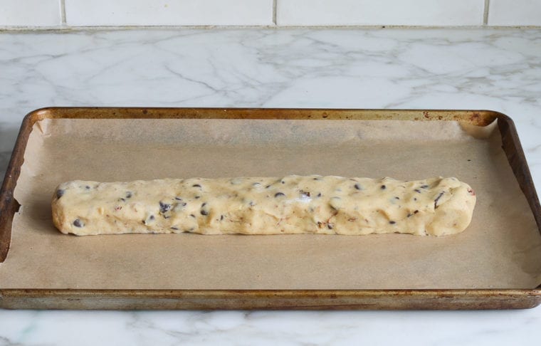 Log of chocolate chip dough on a lined baking sheet.