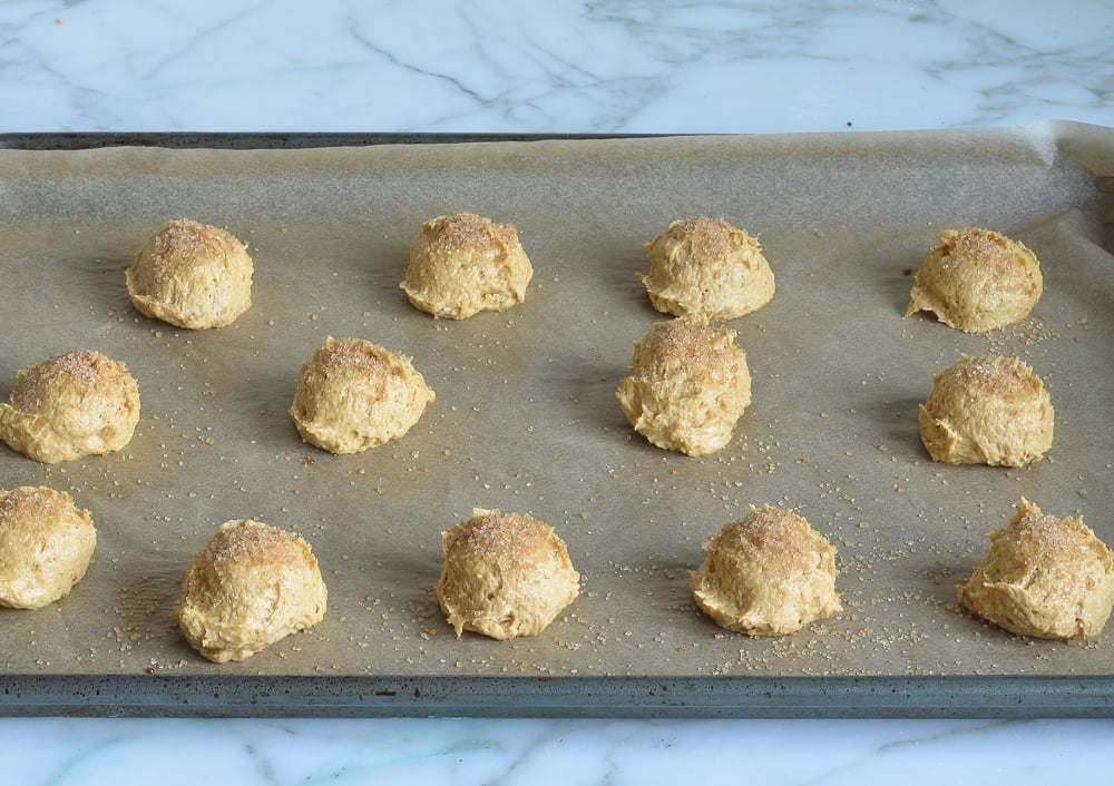 Balls of pumpkin cookie dough on a lined baking sheet.