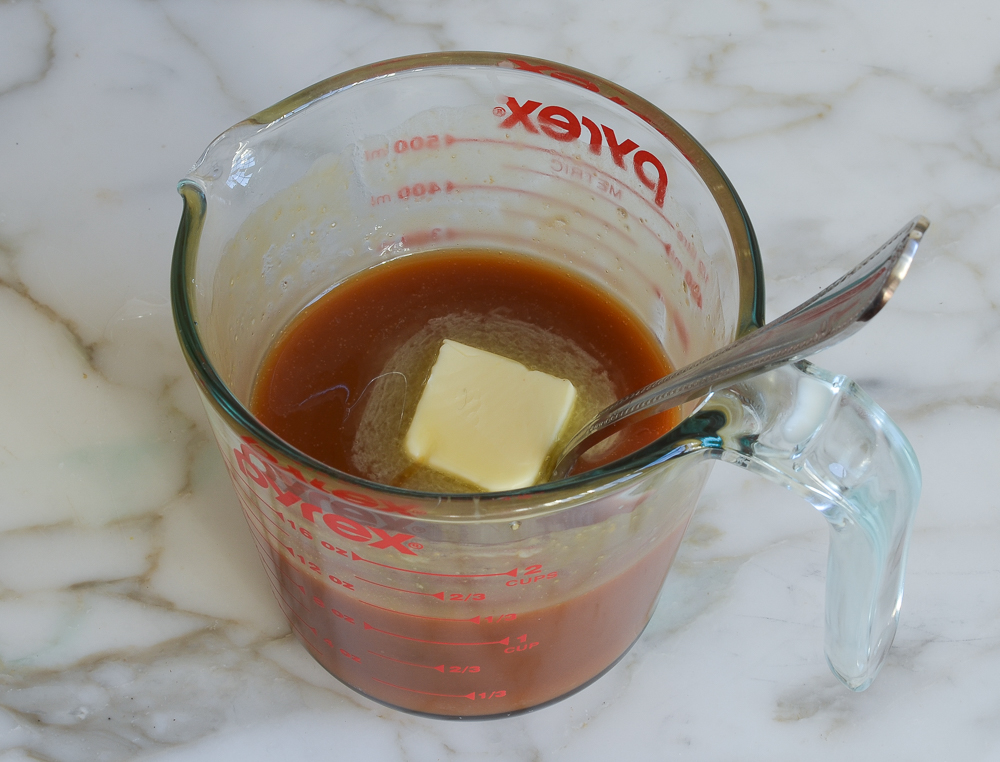 Butter melting into a measuring cup with amber liquid.