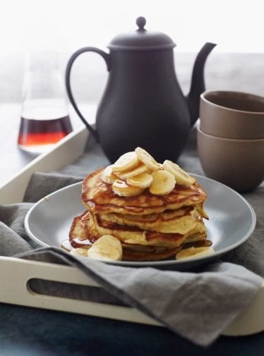 Stack of banana pancakes topped with bananas and syrup.