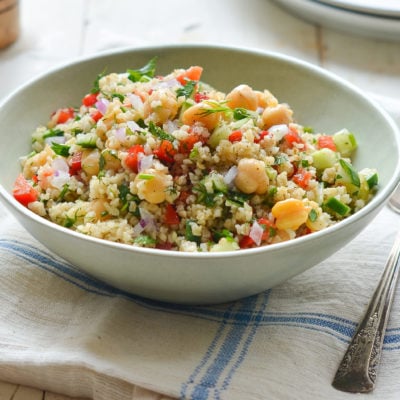 Bowl of bulgur salad with cucumbers, red peppers, chickpeas, lemon, and dill.