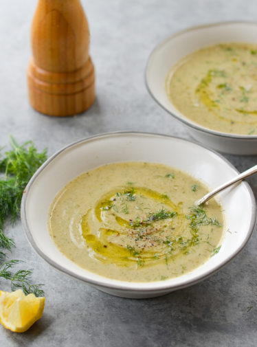 Spoon in a bowl of creamy zucchini soup with walnuts and dill.